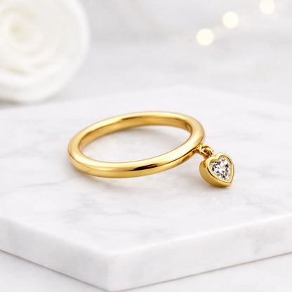 Heart diamond charm ring in solid gold with a floating heart diamond pendant attached to a thin band photo graphed in soft light